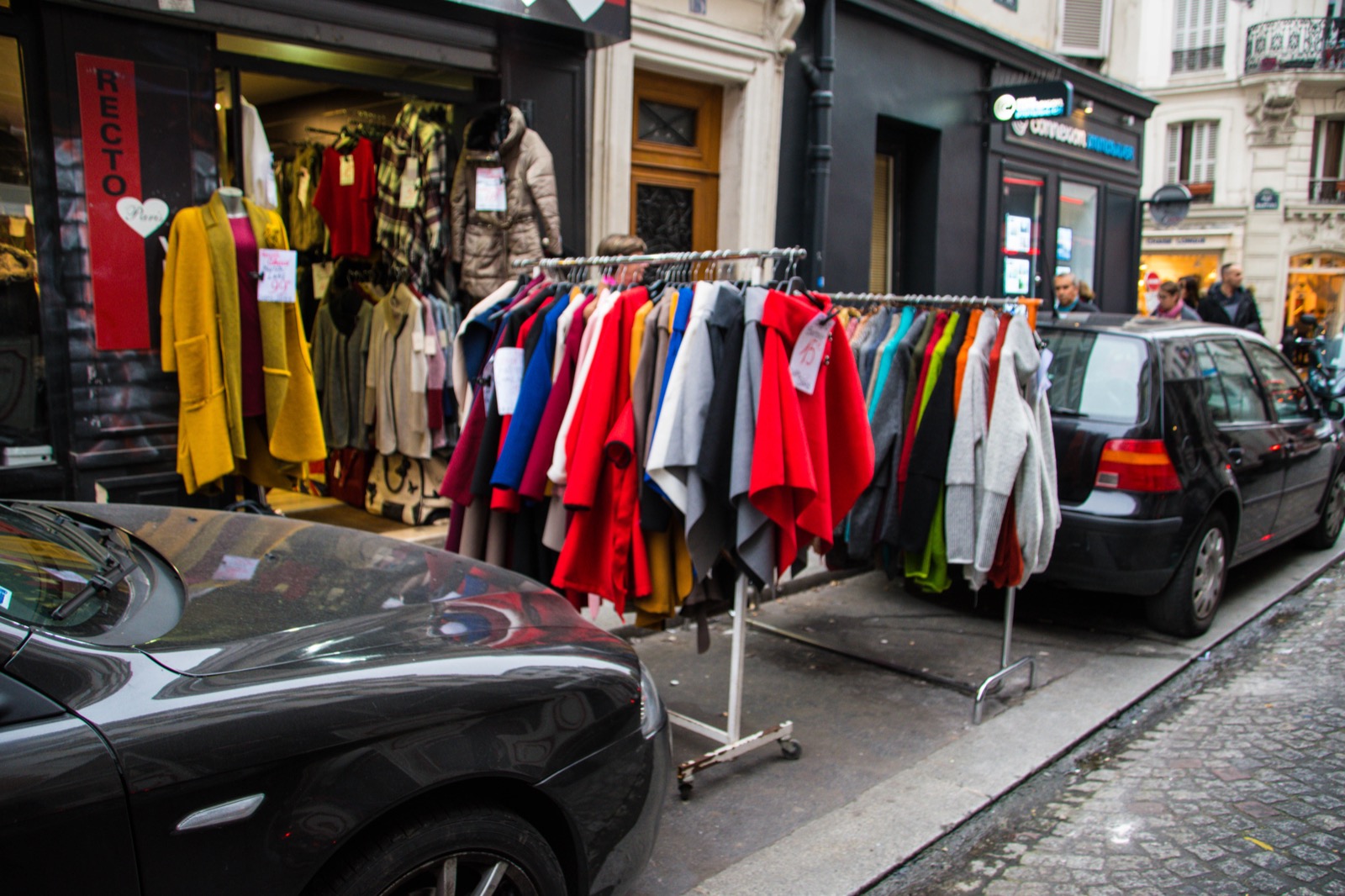 Des portants de vêtements sur le trottoir devant une boutique parisienne