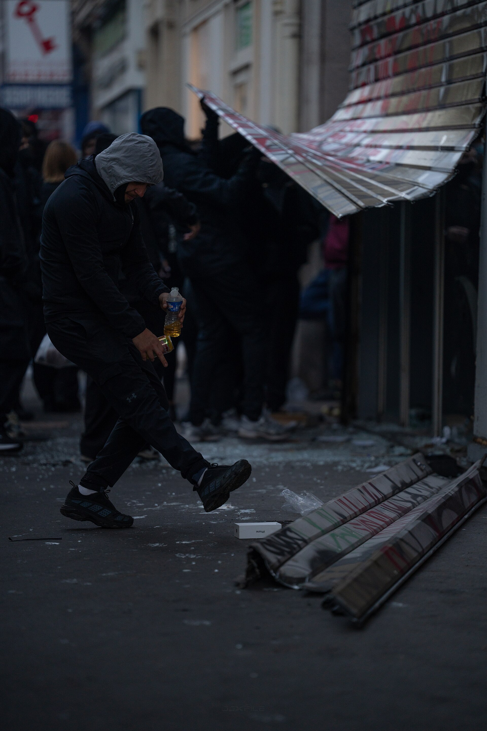 Une personne encapuchonnée devant le rideau déformé d’un commerce parisien.