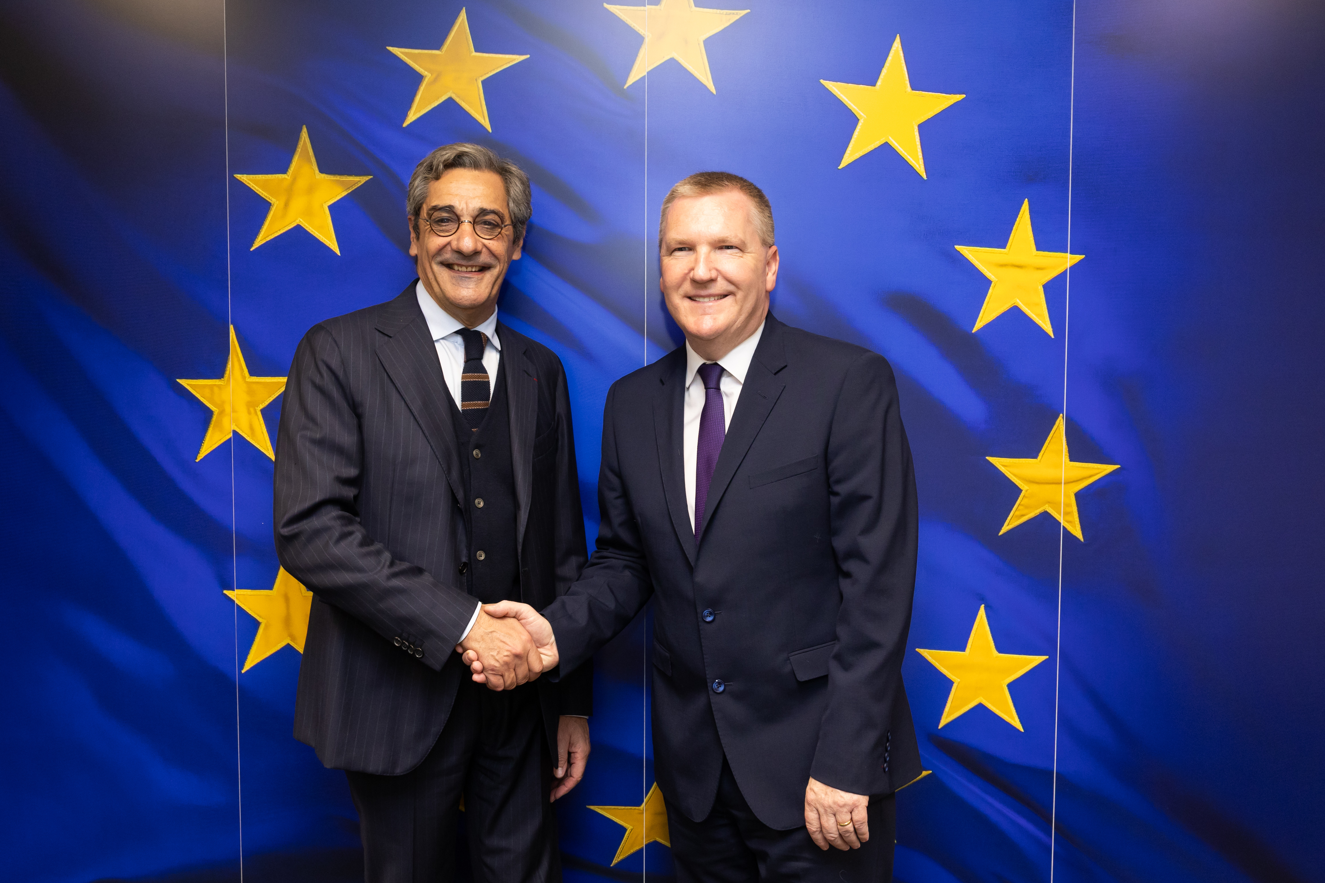 Serge Papin et Michael McGrath se serrent la main devant un fond bleu aux étoiles européennes.
