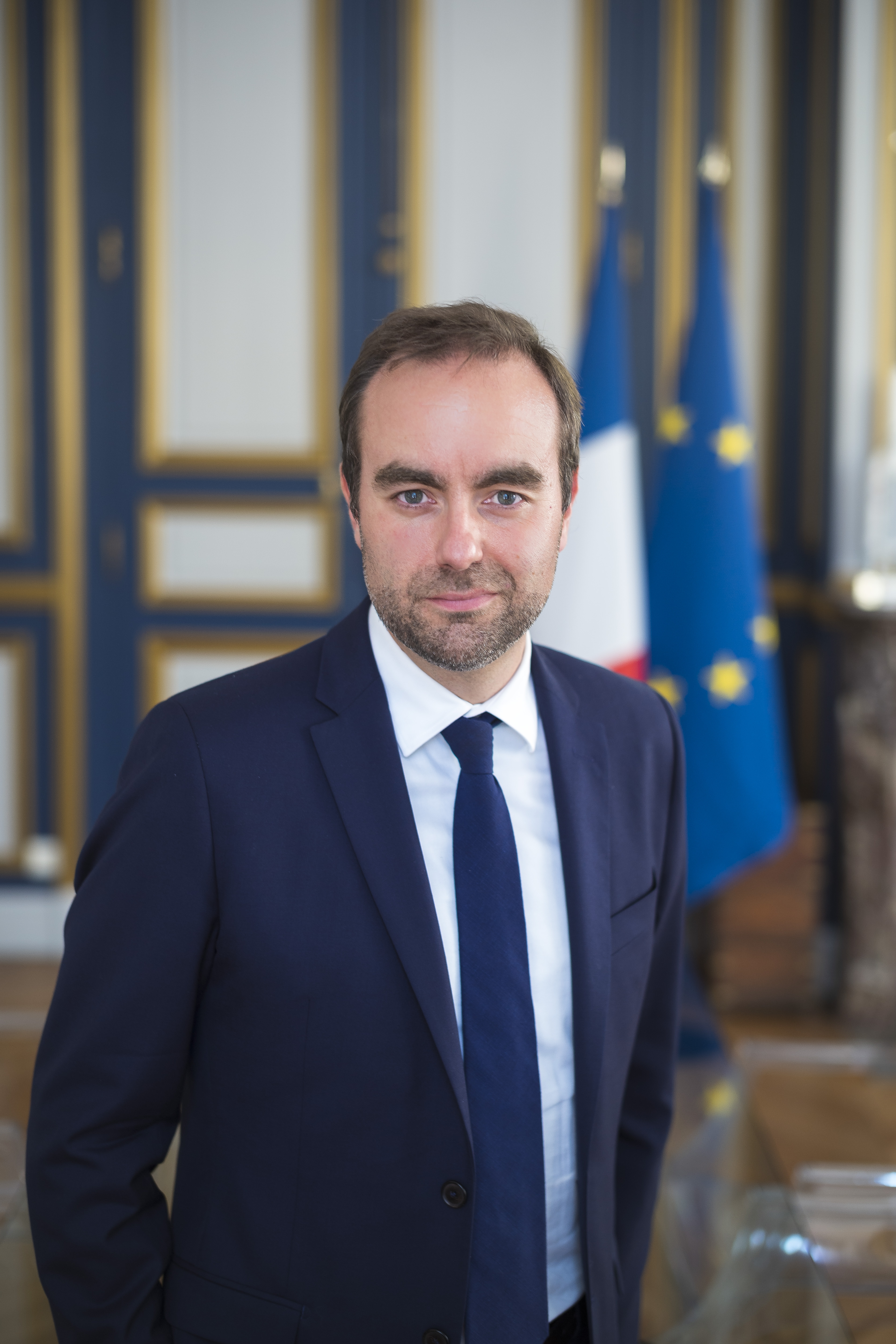 Portrait de Sébastien Lecornu devant des drapeaux français et européen.